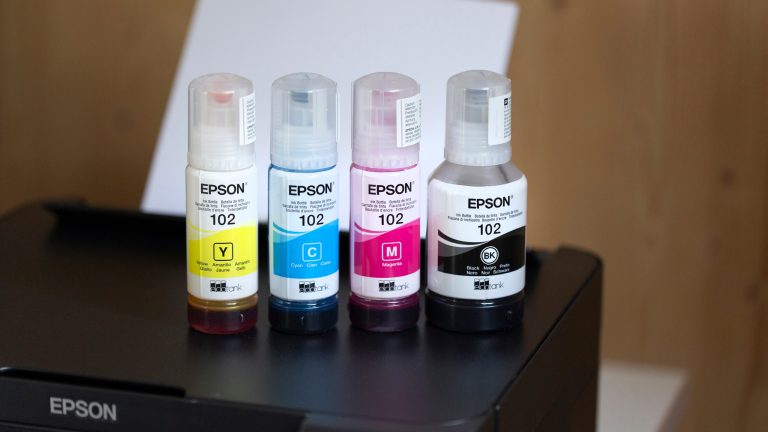 Epson Tintenflaschen in Gelb, Cyan, Magenta und Schwarz stehen auf einem Epson EcoTank Drucker.