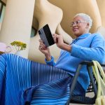 Eine Person sitzt vor einem futuristischen Gebäude auf einem Stuhl an einem Tisch und tippt auf ihrem aufgeklappten Google Pixel 10 Pro Fold.