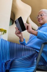 Eine Person sitzt vor einem futuristischen Geb&auml;ude auf einem Stuhl an einem Tisch und tippt auf ihrem aufgeklappten Google Pixel 10 Pro Fold.