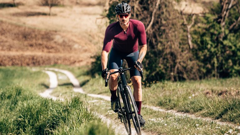 Powermeter, GPS & Co., Tracking für Rennrad und Gravelbike Eine Person fährt in Radsportdress auf einem Gravelbike einen Feldweg im Stehen hinauf.