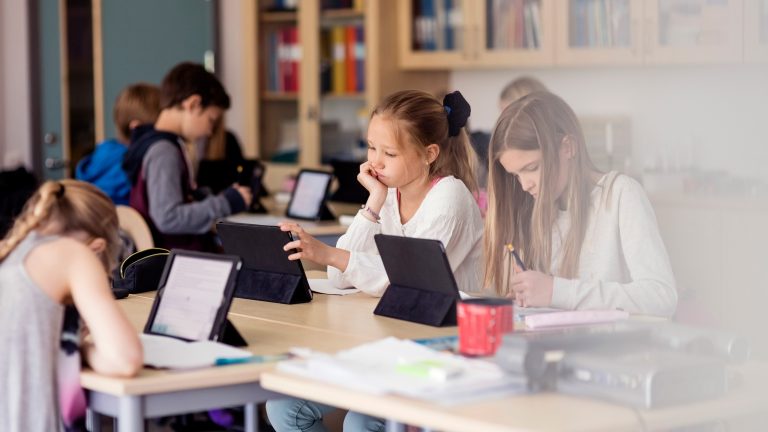 Kinder in einer Schule sitzen an Tischen und bedienen Tablets vor ihnen.