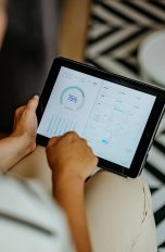 Aufnahme aus der Vogelperspektive einer Person, die ein Tablet in den Händen hält auf dessen Display eine App zur Smarthome-Steuerung geöffnet ist.