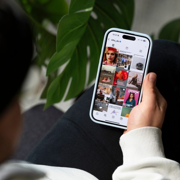 Der Blick &uuml;ber die Schulter einer Person auf ein Handy auf ihrem Bein, das den Instagramfeed von Otto.de zeigt.
