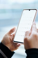 Nahaufnahme von zwei Händen, die ein Smartphone halten. Auf dem Screen erscheint eine geöffnete Kalender-App.