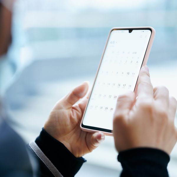 Nahaufnahme von zwei Händen, die ein Smartphone halten. Auf dem Screen erscheint eine geöffnete Kalender-App.