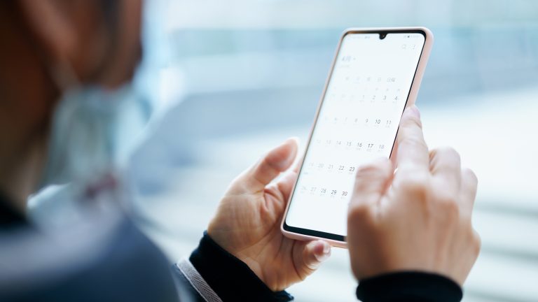 Nahaufnahme von zwei H&auml;nden, die ein Smartphone halten. Auf dem Screen erscheint eine ge&ouml;ffnete Kalender-App.