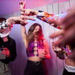 Personen tanzen ausgelassen zu Musik. In den Händen halten sie einen großen Becher.