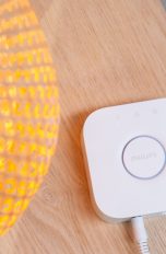 Eine Philips-Hue-Bridge liegt neben einer eingeschalteten Lampe auf einem Tisch.