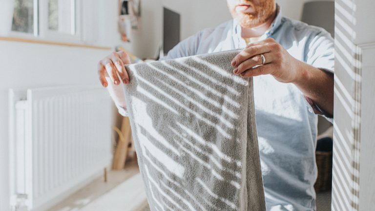 Eine Person steht in einem hellen Raum und faltet ein frisch gewaschenes Handtuch.