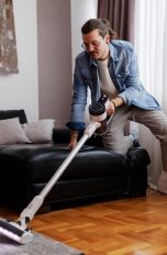Dyson Staubsauger Alternativen, Diese Modelle überzeugen im Alltag Eine Person kniet mit einem Knie auf der Couch, während sie mit einem kabellosen Sauger den Teppich saugt.