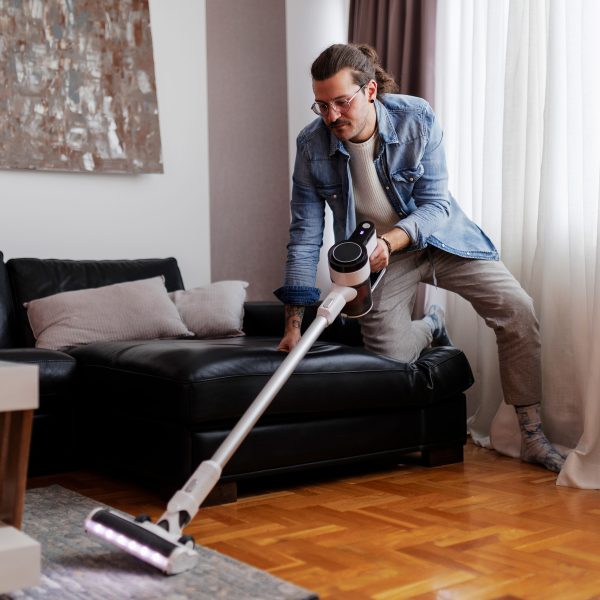 Eine Person kniet mit einem Knie auf der Couch, während sie mit einem kabellosen Sauger den Teppich saugt.