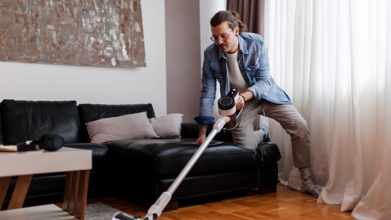 Eine Person kniet mit einem Knie auf der Couch, während sie mit einem kabellosen Sauger den Teppich saugt.