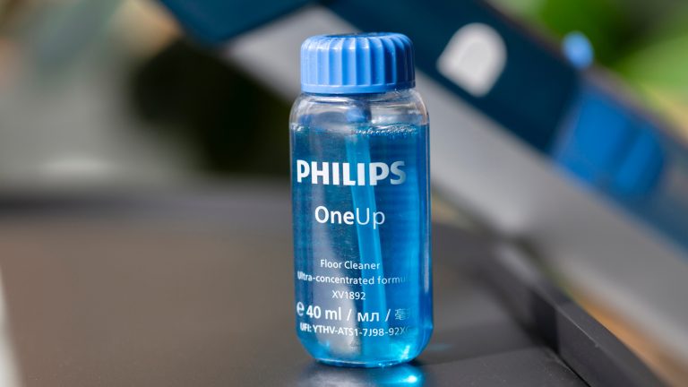 Philips-OneUp-10 Ein Fläschchen Reinungskonzentrat steht auf einem Tisch. Im Hintergrund ist der OneUp zu sehen.