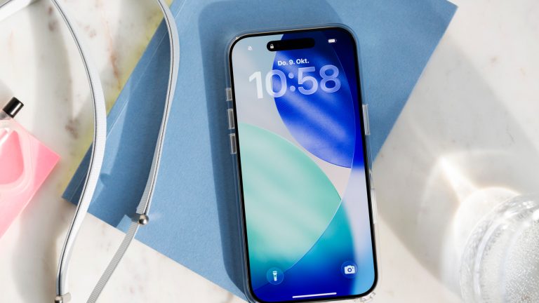 Ein iPhone Air liegt in einer durchsichtigen Schutzh&uuml;lle auf einem Tisch. An der H&uuml;lle ist eine Trageschlaufe angebracht.