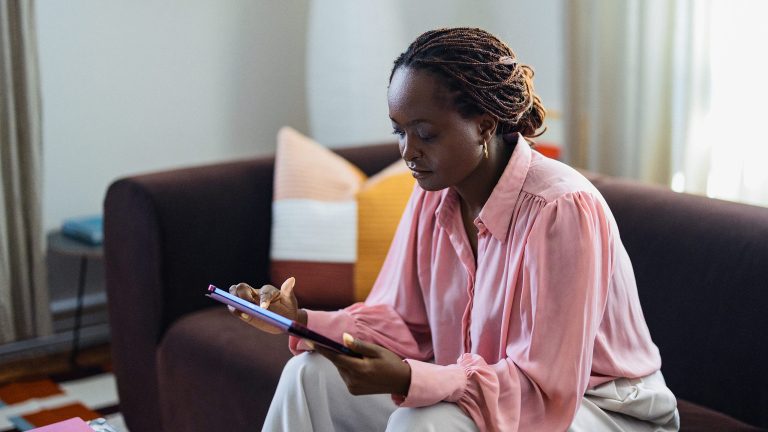 Eine Person sitzt auf einer Couch und hält in beiden Händen ein Tablet vor sich.
