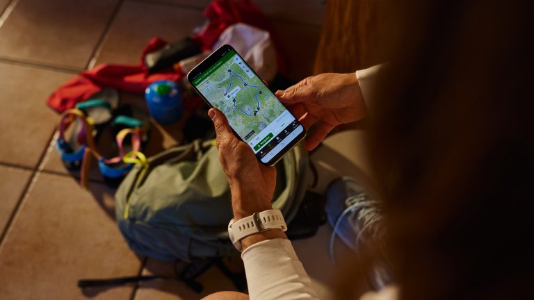 Aufnahme aus der Vogelperspektive einer Person, die ein Smartphone mit ge&ouml;ffneter Komoot-App in den H&auml;nden h&auml;lt.