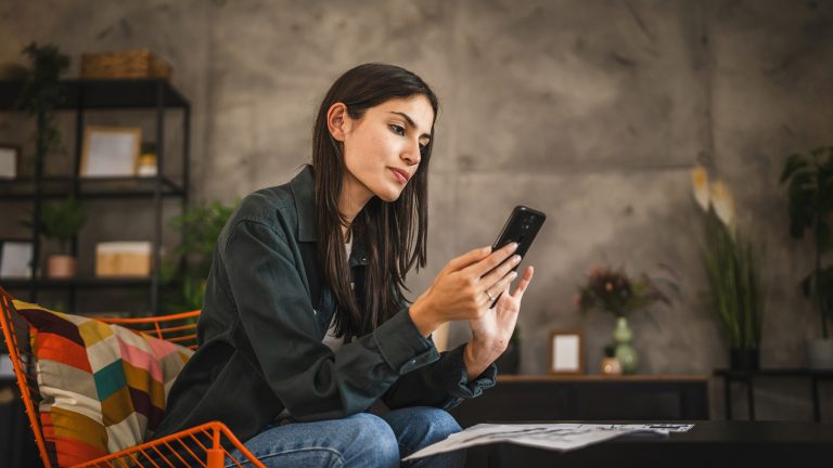 Eine Person sitzt auf einem Stuhl in einem Raum mit ”industrial flair”. In ihren Händen hält sie ein Smartphone.