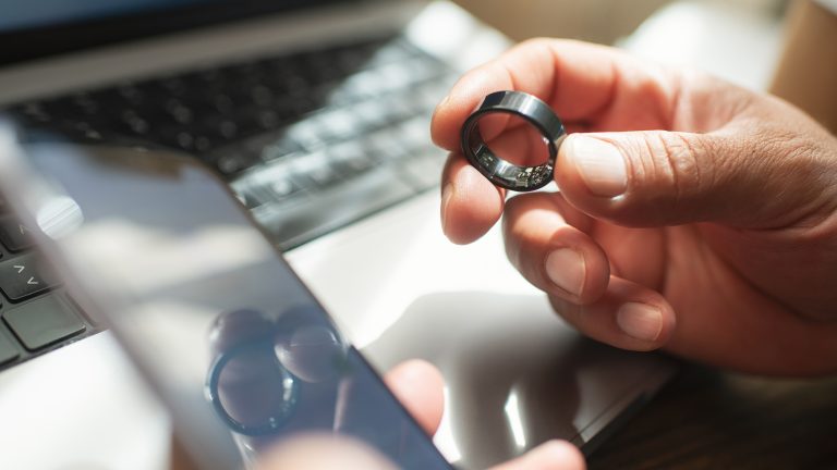 Nahaufnahme zweier Hände. Die linke hält ein Smartphone, die rechte einen Smart Ring. 