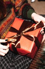 Zu Weihnachten, Geschenke bis rund 100 Euro Vogelperspektive auf eine Person, die vor einem Weihnachtsbaum sitzt und ein Geschenk auf ihrem Schoß hat.