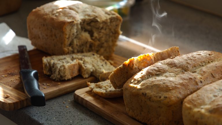 Mehrere frische Brote liegen auf zwei Holzbrettern. Eines davon ist mit einem Messer aufgeschnitten und dampft noch.