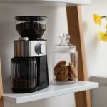 Eine Kaffeem&uuml;hle steht neben einem Vorratsglas mit Cookies in einem Regal.