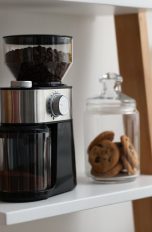 Eine Kaffeem&uuml;hle steht neben einem Vorratsglas mit Cookies in einem Regal.
