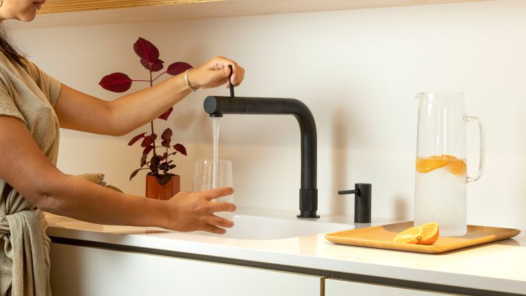 Quooker-Front-schwarz Eine Person gießt Wasser aus einem schwarzen Quooker Front Wasserhahn in ein Glas.