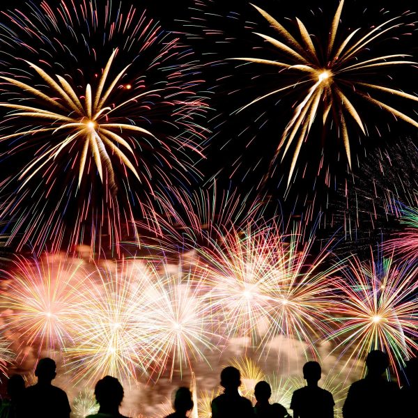 Die dunklen Silhouetten von mehreren Menschen vor einem n&auml;chtlichen Feuerwerk.
