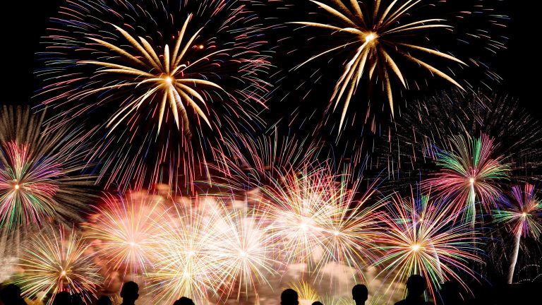 Die dunklen Silhouetten von mehreren Menschen vor einem n&auml;chtlichen Feuerwerk.