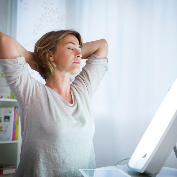 Eine Tageslichtlampe strahlt eine Person von einem Tisch aus an.