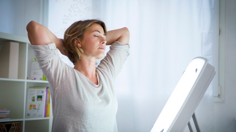 Eine Tageslichtlampe strahlt eine Person von einem Tisch aus an.