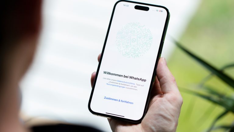 Eine Hand h&auml;lt ein iPhone, auf dem der "Willkommen bei WhatsApp"-Startbildschirm zu sehen ist.