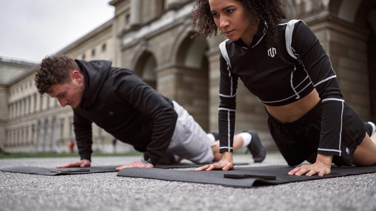 7 Fitness-Apps für Android, Diese Apps unterstützen dich Zwei Personen sind draußen auf Matten und treiben Sport mit Eigengewicht. Vor ihnen liegen Smartphones.