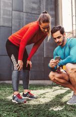 Zwei Personen sind in Sportkleidung auf einem Hinterhof und schauen zusammen auf ein Smartphone.