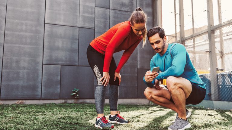 Zwei Personen sind in Sportkleidung auf einem Hinterhof und schauen zusammen auf ein Smartphone.