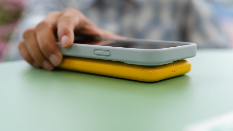 Eine Person legt ein Smartphone auf eine gleich gro&szlig;e Powerbank auf einem Tisch.