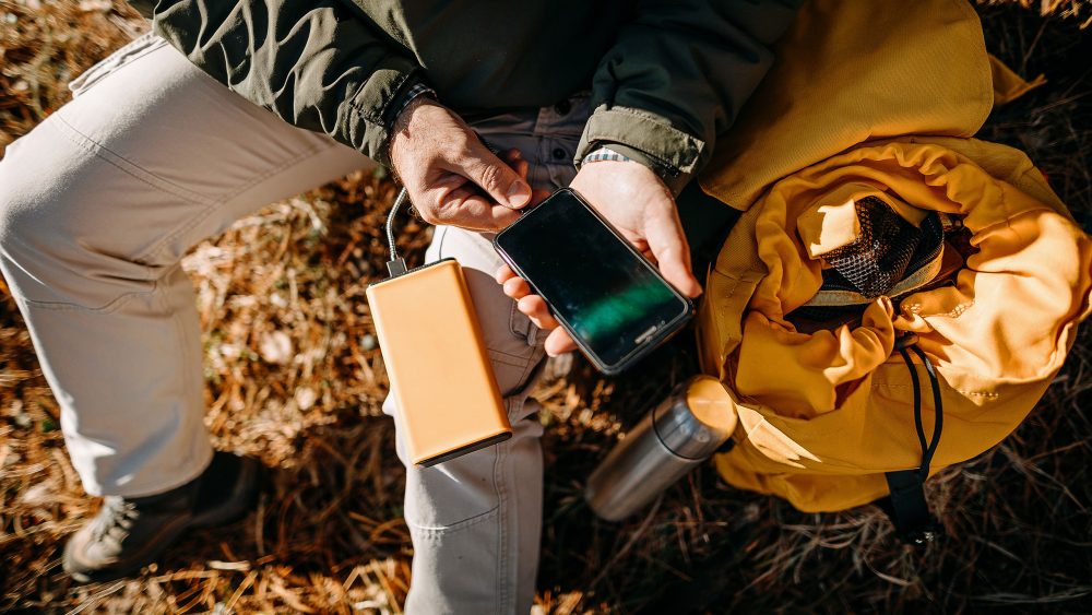 Eine Person sitzt drau&szlig;en und verbindet ihr Smartphone mit einer Powerbank.