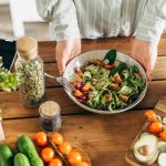 Vogelperspektive auf eine Arbeitsplatte in der K&uuml;che aus Holz auf der ein bunter Salat zubereitet wird.