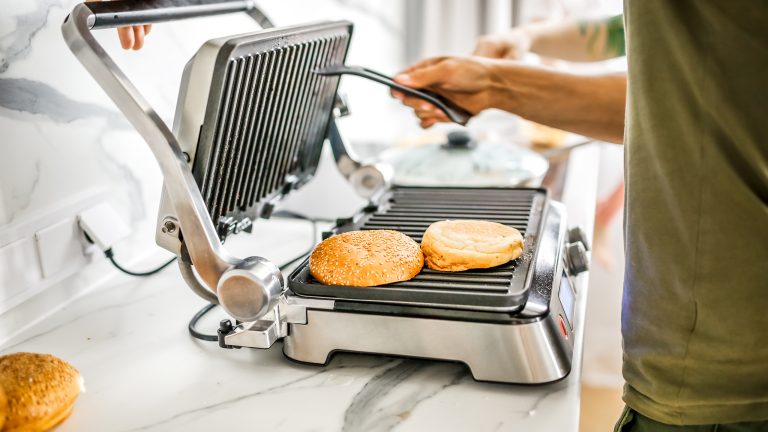 Veganuary, Diese Küchengeräte helfen dir beim veganen Start ins neue Jahr Eine Person ist dabei einen Kontaktgrill zu schließen auf dem Burgerbrötchen liegen.