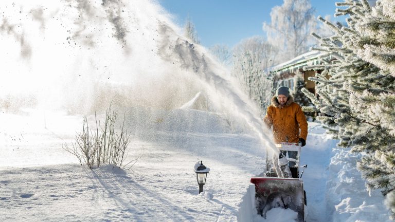 Eine Person in dicken Winterklamotten r&auml;umt im tiefen Schnee einen kleinen Weg frei.