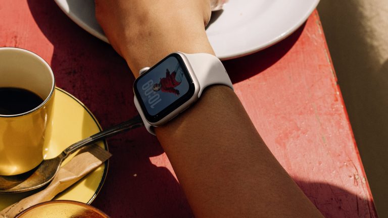 Eine Person sitzt an einem Kaffeetisch. IN der Nahaufnahme ist eine Apple Watch SE 3 zu sehen.