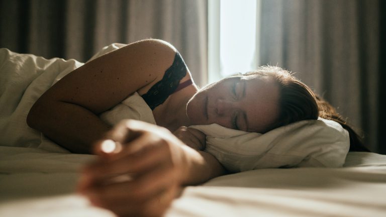 Eine Person liegt in der Seitenschl&auml;ferposition im Bett. Hinter ihr ist der Vorhang leicht ge&ouml;ffnet und l&auml;sst das Tageslicht ins Zimmer scheinen.