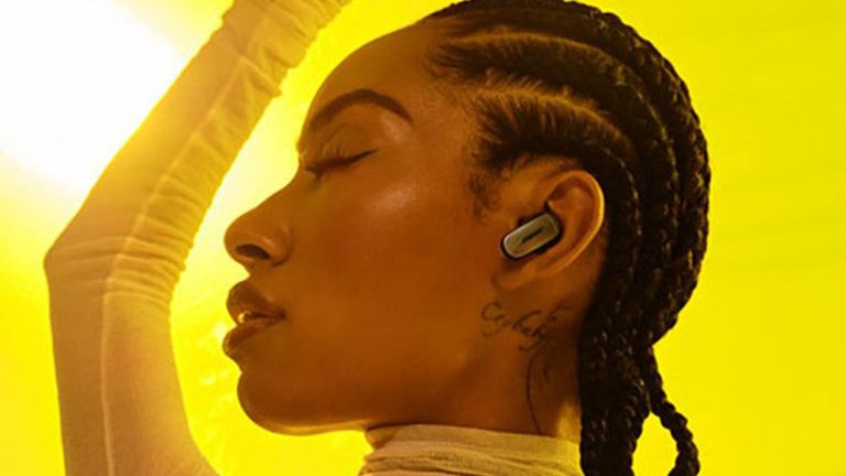 Profilaufnahme einer Person, die in gelblichem Licht steht und die Bose QuietComfort Ultra Earbuds tr&auml;gt.