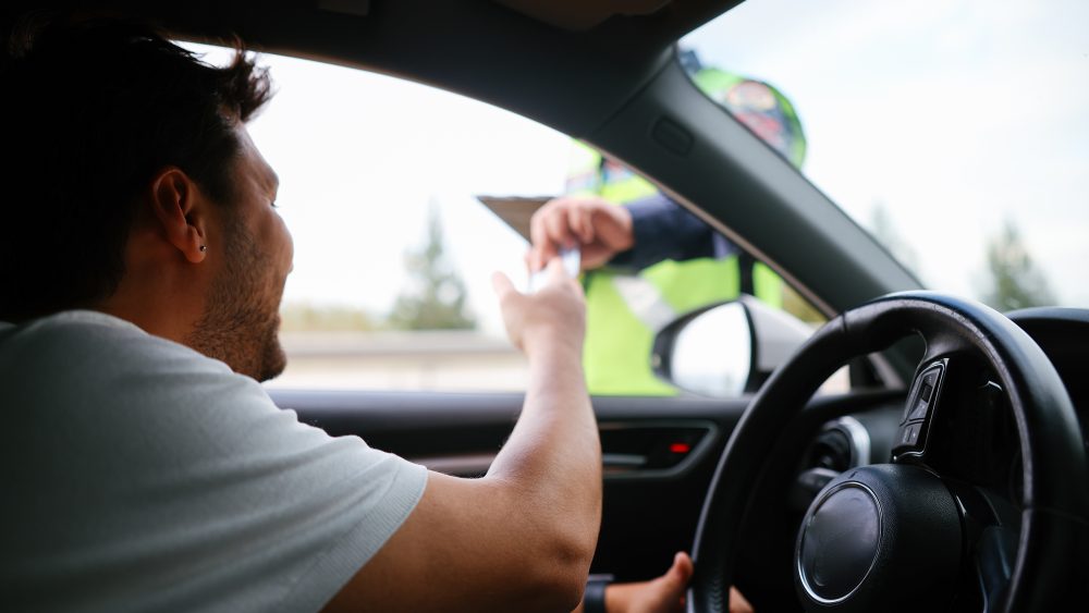 Eine Person ist in eine Fahrzeugkontrolle geraten und reicht der Polizei die Fahrzeugpapiere durchs Fenster.