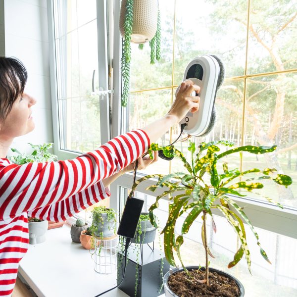 Eine Person reinigt mit einem elektrischen Fenstersauger ein Fenster in ihrem Zuhause.