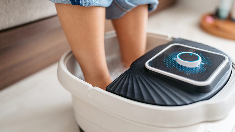 So gelingt dir die perfekte Pediküre zuhause Zwei Füße stecken in einem Fußbad. Die Person trägt hochgekrempelte Jeans.