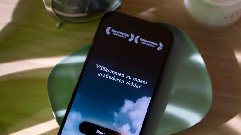 Auf einem iPhone, das auf einer gr&uuml;nen Schale liegt, ist die Startseite der sleep cycle-App ge&ouml;ffnet.