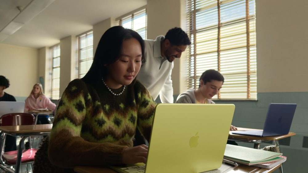 Eine Person sitzt vor einem MacBook Neo in der Farbe Zitrus in eiem Klassenzimmer.