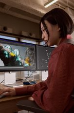 Eine Person sitzt vor einem MacBook Pro + Studio Display an einem Schreibtisch vor einem Fenster.