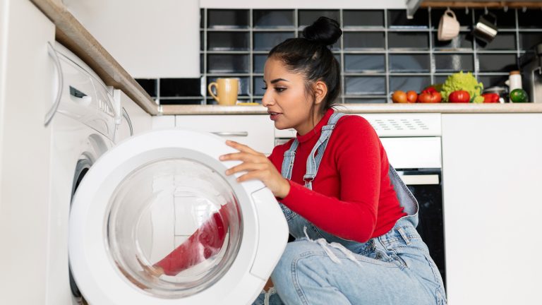 Eine Person ist vor einer Waschmaschine in der Hocke und l&auml;dt W&auml;sche in das Ger&auml;t.